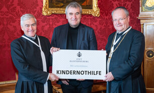 Stiftskämmerer Elias Carr Can.Reg., Kindernothilfe-Österreich Geschäftsleiter Gottfried Mernyi, Propst Anton Höslinger Can.Reg. halten gemeinsam einen symbolischen Scheck