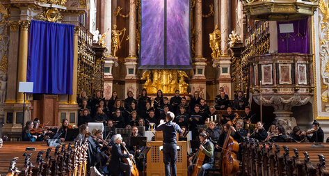 Prunkvolle Stiftskirche mit Orchester und Dirigent und lila verhülltem Altar.