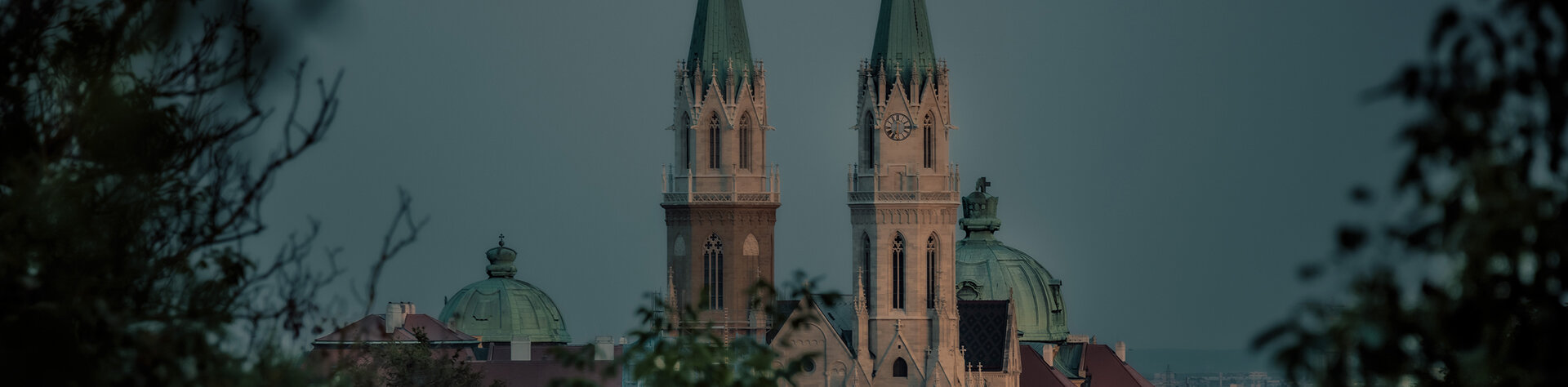 Die Türme der Stiftsbasilika Klosterneuburg umrahmt von Blättern mit aufgehendem Mond.