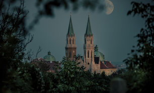 Die Türme der Stiftsbasilika Klosterneuburg umrahmt von Blättern mit aufgehendem Mond.
