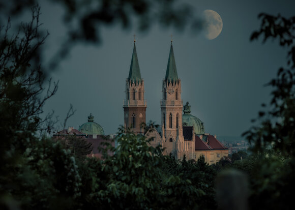 Die Türme der Stiftsbasilika Klosterneuburg umrahmt von Blättern mit aufgehendem Mond.