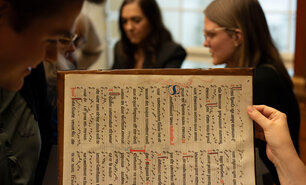 Person hält eine alte Handschrift hoch, im Hintergrund schauen mehrere Menschen zu.