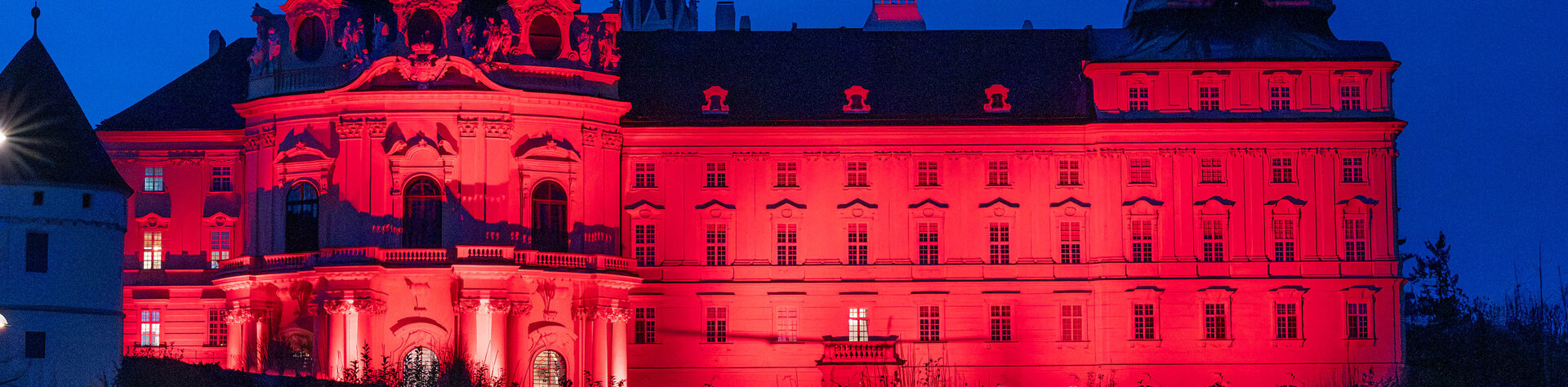 Die ro beleuchtete barocke Fassade des Stiftes Klosterneuburg im dunkelblauen Nachthimmel