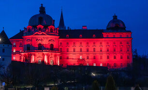Die ro beleuchtete barocke Fassade des Stiftes Klosterneuburg im dunkelblauen Nachthimmel