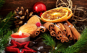 Weihnachtliches Stillleben mit Zimtstangen, Walnüssen, getrockneten Orangenscheiben, einer roten Kerze, Tannenzweigen und Dekorationen auf Holzuntergrund.