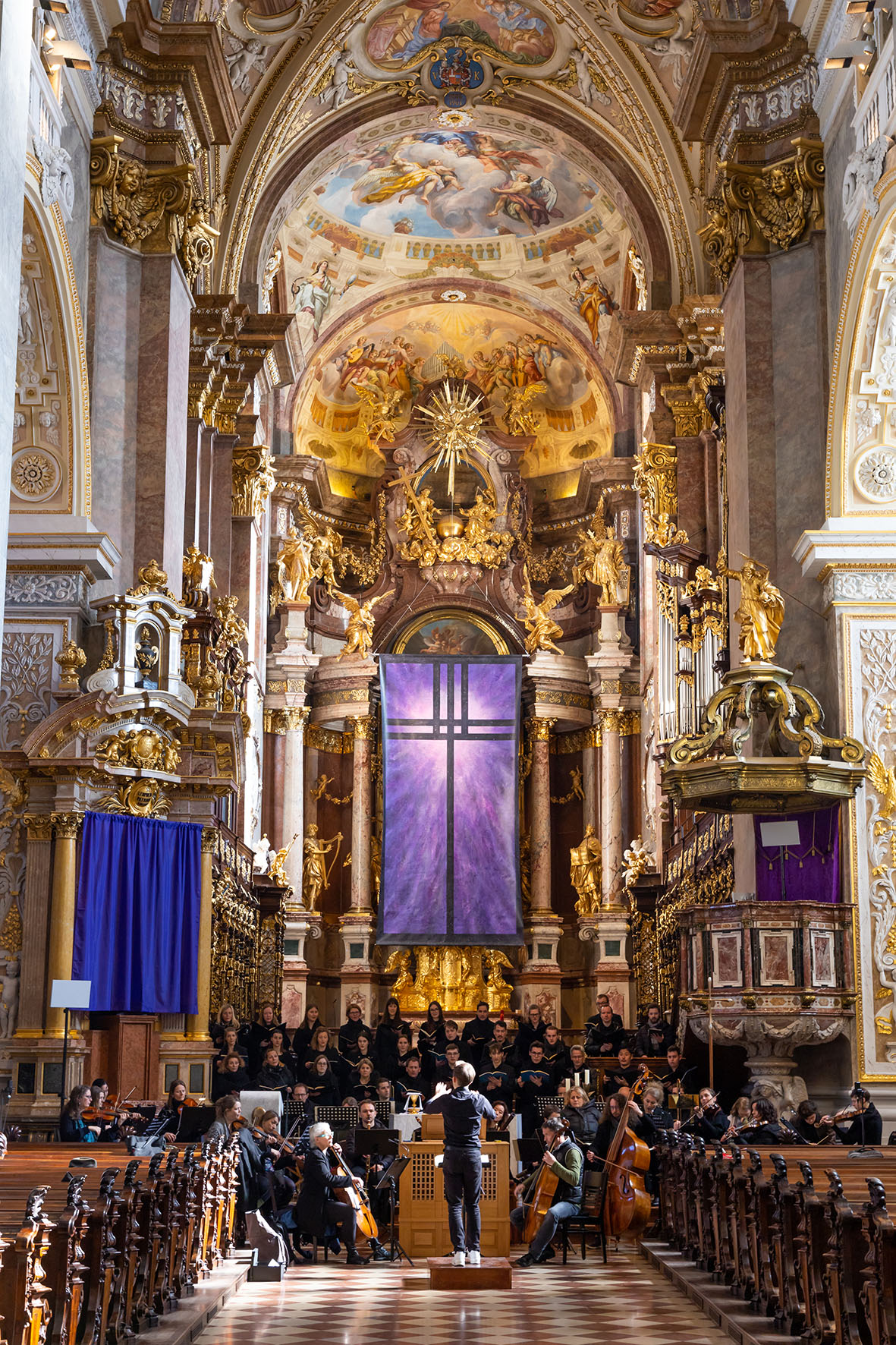 Prunkvolle Stiftskirche mit Orchester und Dirigent und lila verhülltem Altar.
